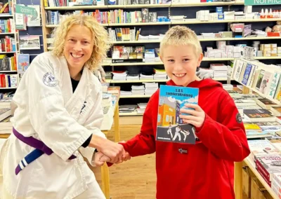Charlotte Doornhein in reikt in jiu-jitsu tenu met paarse band, haar boek uit aan een jonge lezer in de boekhandel.